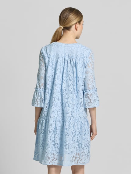 Frauenmodel trägt Loose Fit Spitzenkleid aus Baumwoll-Mix Modell 'HONEY' von Vero Moda, Optik: Unifarben, Spitzen-Muster, knielang, V-Ausschnitt, 3/4-Arm mit Glockenärmel, Materialverarbeitung: Spitze, Farbe Hellblau, Ganzkörperansicht Rückansicht.