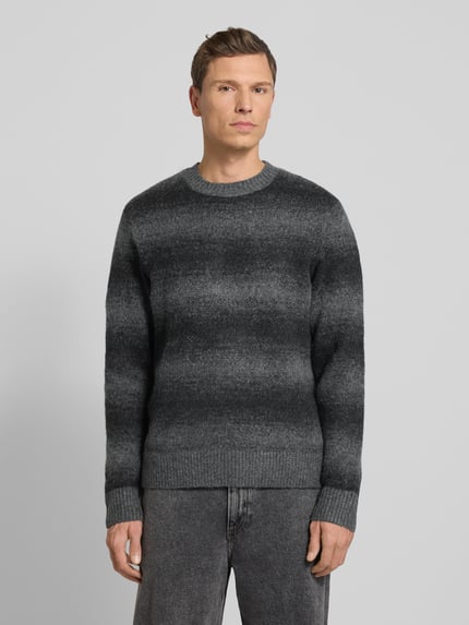 Männermodel trägt Strickpullover mit Rundhalsausschnitt von Jack & Jones Premium im Grau-Schwarz Material-Mix mit Woll-Anteil, lockerer Schnitt, gerippte Abschlüsse, Ganzkörperansicht von vorne.