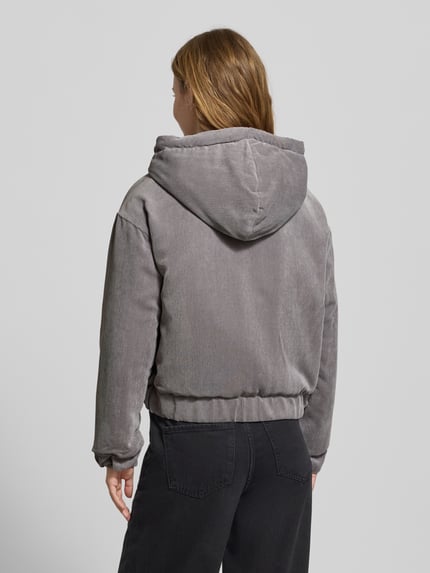 Frauenmodel trägt Regular Fit Bomberjacke mit Kapuze Modell 'SUVA' von Only aus grauem Cord mit Label Stitching, Ganzkörperansicht Rückansicht.