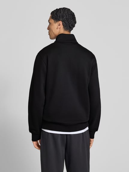 Männermodel trägt schwarzes Sweatshirt mit Label-Details von Champion, Troyer-Kragen, seitliche Eingrifftaschen, Rückenansicht, Baumwollmischung.