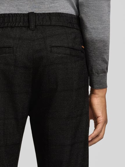 Männermodel trägt Tapered Fit Chino mit Viskose-Anteil von BOSS Orange in Dunkelgrau mit feinem Karomuster, Nahaufnahme Rückansicht.