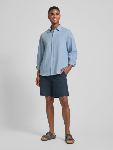 Männermodel trägt Regular Fit Freizeithemd aus Leinen-Baumwoll-Mix Modell 'CLAY LINENBLEND' von SELECTED HOMME in Melange-Optik, Kentkragen, durchgehende Knopfleiste, langarm, 2-Knopf-Manschette, Rückenpasse, Flammgarn Materialverarbeitung, leicht abgerundeter Rumpfabschluss, Ganzkörperansicht von vorne.