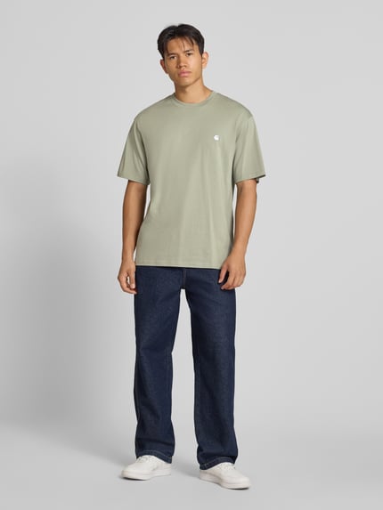 Männermodel trägt Regular Fit T-Shirt aus reiner Baumwolle Modell 'Madison' von Carhartt Work In Progress, dezentes Grün, Ganzkörperansicht von vorne. Herren T-Shirt mit Rundhalsausschnitt, Label-Stitching, Rückenlänge bei Größe M 78 cm, glatte Struktur.