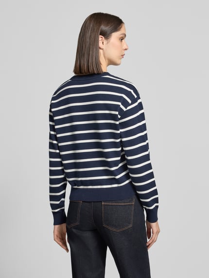 Frauenmodel trägt Pullover mit Knöpfen am Schulterabschluss von Tommy Hilfiger in dunkelblauer Strickoptik mit weißen Streifen, gerippte Abschlüsse, Ganzkörperansicht Rückansicht.