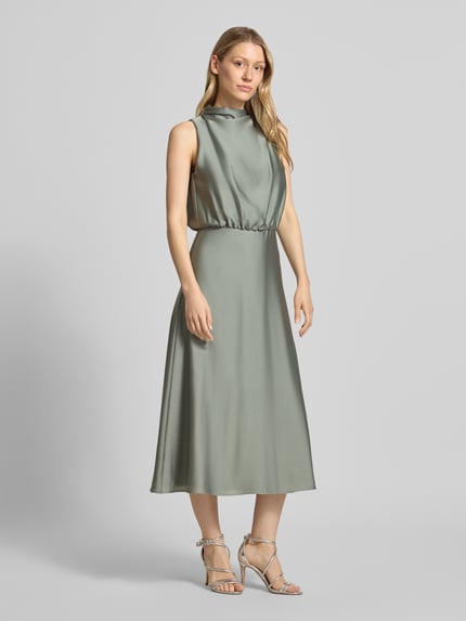 Frauenmodel trägt Cocktailkleid mit Stehkragen von Swing in sanftem Grün, Midikleid, glatte Textur, Ganzkörperansicht von vorne. Taillierte Passform, Reißverschluss hinten, Unterkleid, Rückenlänge 126 cm, Brustweite 34 cm.