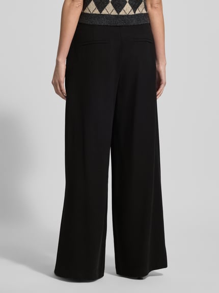 Frauenmodel trägt Hose aus Viskose-Mix mit weitem Bein von MAC in Schwarz mit Gesäßtaschen, Gelegte Falten, Ganzkörperansicht Rückansicht. Bundweite bei Größe 36/32: 40 cm, Innenbeinlänge: 81 cm.