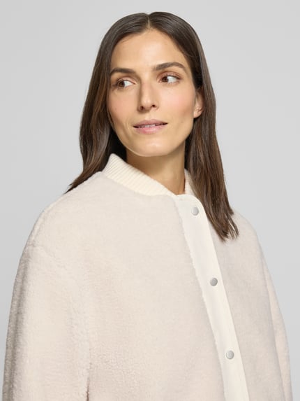 Kobiece modelka nosi kurtkę z polaru z listwą guzikową Model 'Hulda' od OPUS, krój relaxed fit, stójka, zamek błyskawiczny, kremowa faktura, zbliżenie na górę ciała.