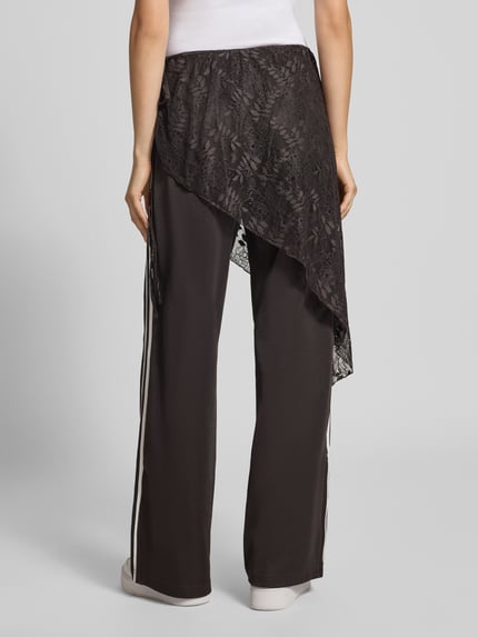 Männermodel trägt schwarze Loose Fit Sweathose aus Baumwoll-Mix Modell '2IN1 LACE FIREBIRD' von adidas Originals, asymetryczna koronka, Ganzkörperansicht Rückansicht.