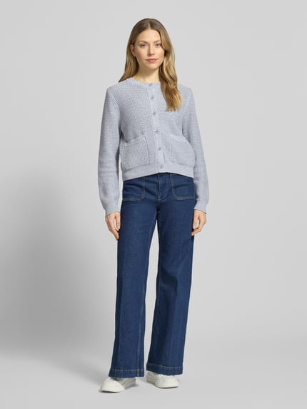 Frauenmodel trägt Regular-Fit Strickjacke mit aufgesetzten Taschen Modell 'Biaphy' von Drykorn aus reiner Baumwolle, Rundhalsausschnitt, Knopfleiste und elastische Abschlüsse, Rückenlänge bei Größe S 50 cm, Ärmellänge 65 cm, hellgraue Struktur, Grobstrick, Vorderansicht Ganzkörperansicht.