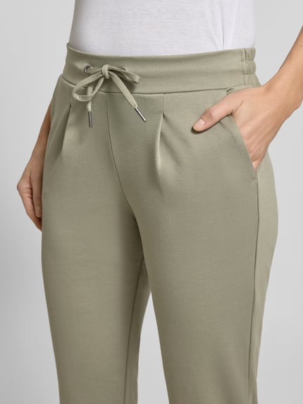 Frauenmodel trägt Slim Fit Stoffhose mit Viskose-Anteil Modell 'Rizet' von B.Young in hellem Khaki, mit elastischem Bund, Bundfalten, 7/8-Länge, Nahaufnahme Hüftbereich. Elastischer Material-Mix, Bundweite 37 cm, Innenbeinlänge 68 cm.