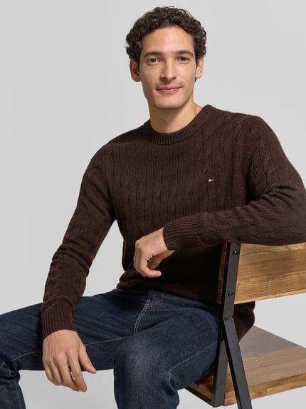 Männermodel trägt Regular Fit Pullover aus reiner Schafswolle von Tommy Hilfiger in Dunkelbraun mit Zopfmuster, Nahaufnahme Oberkörper