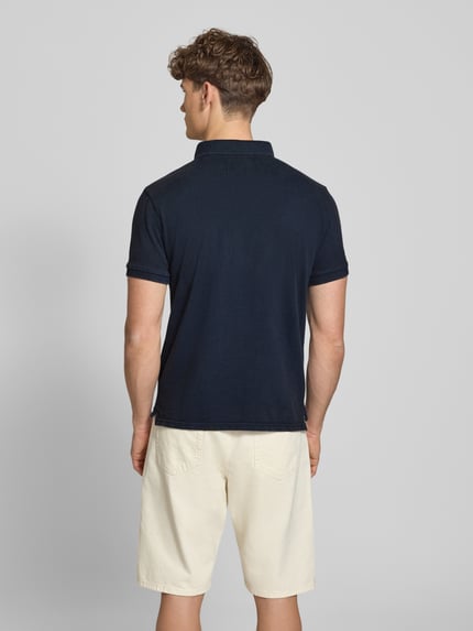 Männermodel trägt Regular Fit Poloshirt mit Logo-Stitching von Superdry aus Reine Baumwolle, Polokragen, Kurzärmelig, Rückenlänge 67 cm, Ganzkörperansicht Rückansicht.