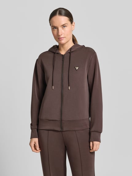 Vrouwenmodel draagt sweatjack met capuchon model 'OLYMPE' van Guess Activewear, materiaalmix met modal, regular fit, labelapplicatie, ritssluiting, kleur bruin, structuur glad, voorkant van het bovenlichaam in beeld.