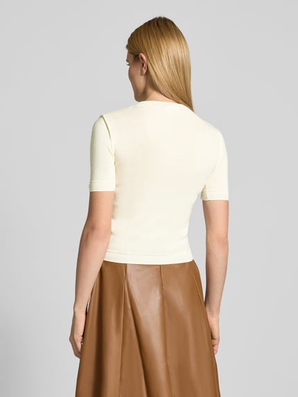 Frauenmodel trägt Slim Fit Strickshirt mit Woll-Anteil Modell 'CAROLINE' von Guido Maria Kretschmer WOMAN, Material-Mix, Stehkragen, 1/2-Arm, Farbe Creme, kombiniert mit braunem Rock, glatte Textur, Ganzkörperansicht Rückansicht.