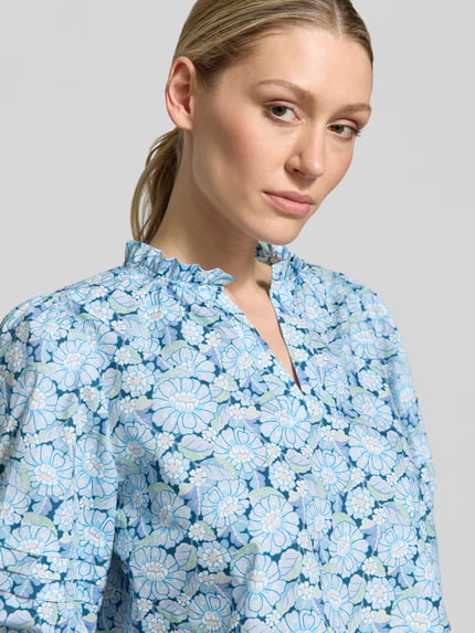 Vrouwenmodel draagt blouse met Serafino-kraag en ballonmouwen van Rich & Royal, puur katoen, loose fit, blauwe bloemenprint, nahaufnahme bovenlichaam.
