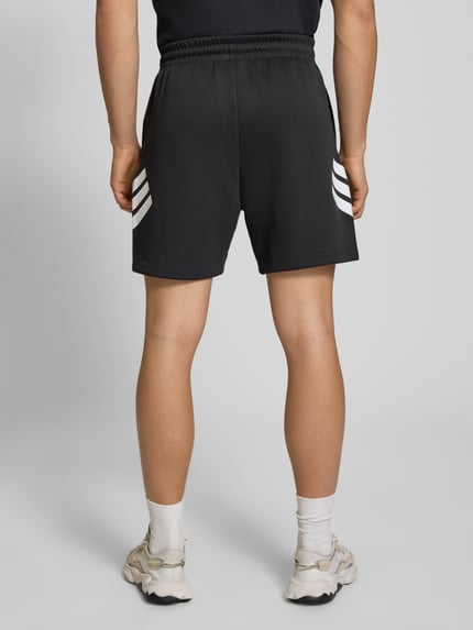 Männermodel trägt Regular Fit Sport-Shorts mit Logo-Print von adidas Sportswear, unifarben, elastischer Bund, seitliche Taschen, Ganzkörperansicht Rückansicht.