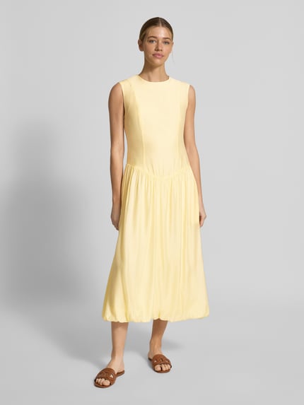 Frauenmodel trägt Bubble Kleid mit Rundhalsausschnitt Modell 'KRISSI' von YAS in gelb, Material-Mix mit Lyocell-Anteil, Taillierter Schnitt, Midikleid, Rückseitiger Reißverschluss, Rückenlänge bei Größe 36: 45 cm, Brustweite bei Größe 36: 43 cm, Ganzkörperansicht von vorne.