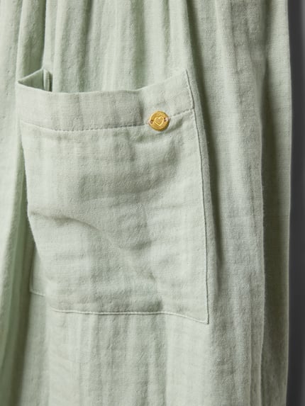 Produktfoto, detal zielonego materiału z fakturą, widoczna nakładana kieszeń i złoty guzik, sukienka 'Knielanges Kleid mit Schmetterlingsärmeln' od Blue Seven, bawełna, luźny krój, długość do kolan, okrągły dekolt, rękawy-motylki, wpuszczane kieszenie, zapięcie na guzik z tyłu, długość tyłu w rozmiarze 116: 65 cm.
