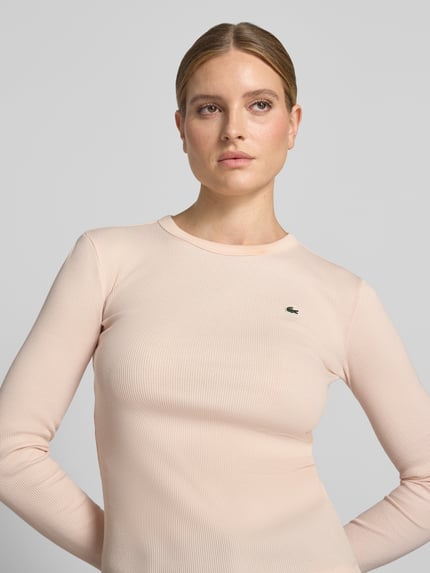 Frauenmodel trägt Slim Fit Langarmshirt aus reiner Baumwolle von Lacoste, zartrosa Farbe, dezente Rippenstruktur, Nahaufnahme Oberkörper, Damen T-Shirt von Lacoste