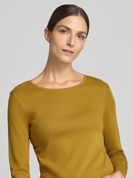 Frauenmodel trägt Slim Fit Longsleeve aus reiner Baumwolle von Christian Berg Woman in Ockergelb, glatte Textur, Nahaufnahme Oberkörper. Damen Longsleeve, taillierte Passform, Rundhalsausschnitt, Rückenlänge bei Größe S 59 cm.