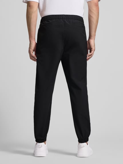Männermodel trägt Slim Fit Schlupfhose mit Gesäßtasche von CK Calvin Klein, schwarze Farbe, elastischer Bund, Ganzkörperansicht Rückansicht.