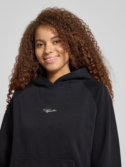 Frauenmodel trägt Hoodie mit Label-Stitching von Pegador aus Baumwoll-Mix, lockerer Schnitt, Kapuze, Känguru-Tasche, gerippte Abschlüsse, Nahaufnahme Oberkörper.