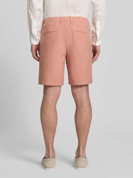Männermodel trägt Regular Fit Bermudas aus Baumwoll-Mix Modell 'KARL' von SELECTED HOMME, seersucker-Textur, hellrosa, Ganzkörperansicht Rückansicht.