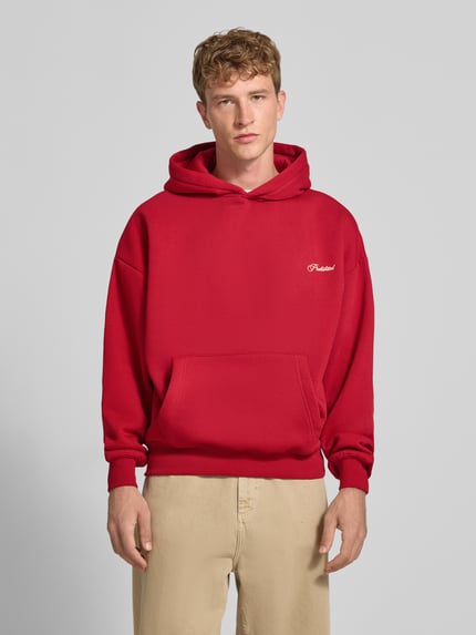 Männermodel trägt Relaxed Fit Hoodie aus Baumwoll-Mix mit Label-Stitching von PROHIBITED, Känguru-Tasche, rot, Ganzkörperansicht von vorne.
