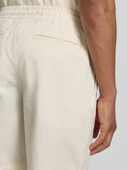 Männermodel trägt Loose Fit Shorts aus Baumwoll-Mix von Lacoste in weiß mit feiner Seersucker-Struktur, Nahaufnahme Rückansicht. Optik:Allover-Muster, Passform: Regular-Fit, Muster: Gestreift, Applikation: Label-Stitching, Bundabschluss: elastisch mit Tunnelzug, Taschen: seitliche Eingrifftaschen, Materialverarbeitung: Seersucker, Material: Baumwoll-Mix.