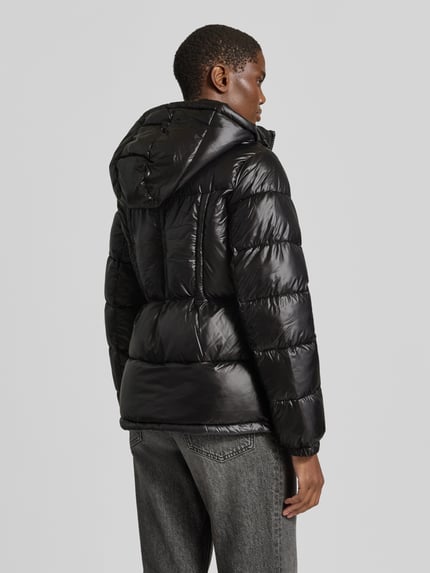 Männermodel trägt Regular Fit Steppjacke mit Logo-Emblem von MICHAEL Michael Kors, schwarz, glänzende Stepp-Optik, Rückenansicht, Ganzkörperansicht Rückansicht. Herren Steppjacke mit Kapuze, Zipper, elastische Ärmelabschlüsse, Eingrifftaschen, Steppstruktur, glatte Textur.