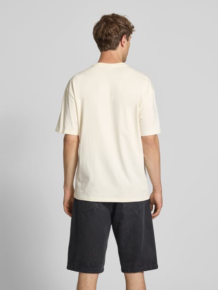 Männermodel trägt Oversized T-Shirt mit Logo-Stitching von KARL KANI, czysta bawełna, krój oversized fit, kremowy, widok całej sylwetki z tyłu.