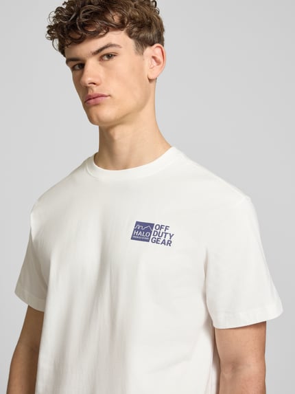 Męski model nosi T-Shirt mit Label-Print od HALO, biała bawełna, krój regular fit, okrągły dekolt, nadruk z przodu, zbliżenie na górną część ciała.