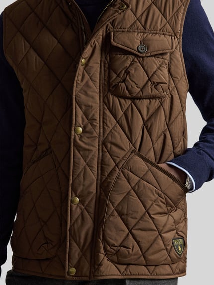 Mężczyznamodel nosi brązową kamizelkę model 'Regular Fit Weste mit Logo-Patch Modell 'BEATON'' od Polo Ralph Lauren, pikowana struktura, naszywka z logo, zbliżenie na górną część ciała, kamizelka Herren Polo Ralph Lauren.