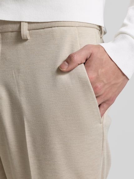 Männermodel trägt Stoffhose mit Gesäßtaschen von MCNEAL in Beige, Material-Mix mit Viskose, sichtbare Bundfalten, Nahaufnahme Hüfte und Hand.