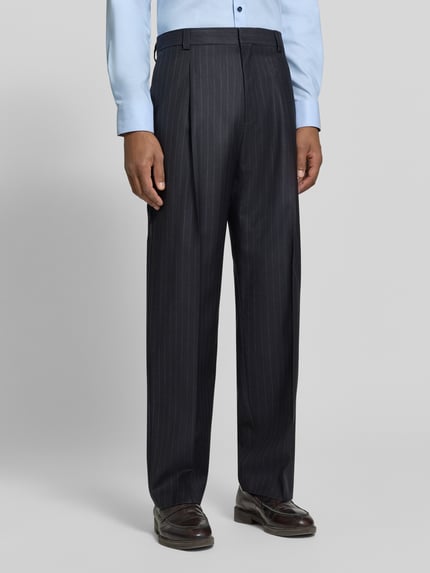 Männermodel trägt Regular Fit Bundfaltenhose aus Wolle von HUGO mit Nadelstreifen, Webware, Bundfalte und Gürtelschlaufen, Ganzkörperansicht von vorne.