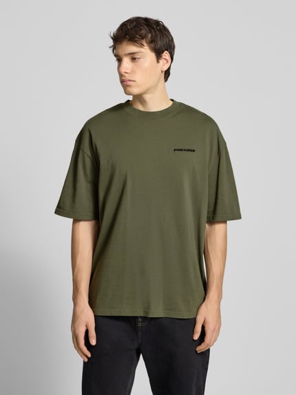 Männermodel trägt Oversized T-Shirt mit Label-Stitching van Pegador in olijfgroen, puur katoen, ribkraag, voorkant, bovenlichaam close-up.