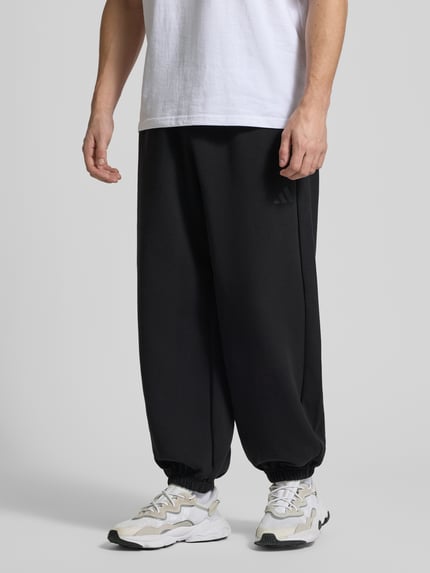 Männermodel trägt Comfort Fit Sweatpants mit Logo-Print von adidas Sportswear, Optik: Unifarben, Materialverarbeitung: Sweat, Ganzkörperansicht von vorne.
