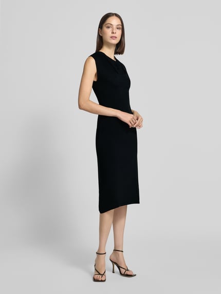 Frauenmodel trägt schwarzes Strickkleid mit Wasserfall-Ausschnitt Modell 'SANTA' von MANGO, gerader Schnitt, Midikleid, Ganzkörperansicht von vorne.