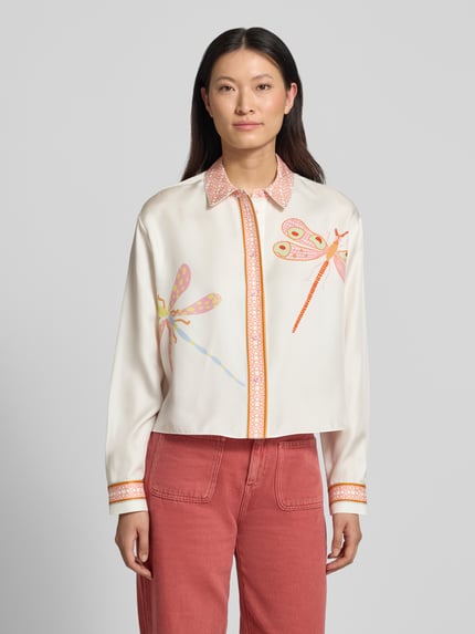 Modelka nosi Regular Fit Bluse im Allover-Look von HERZENS w kremowym kolorze z kolorowymi ważkami, kołnierz koszulowy, zapięcie na guziki, długość tyłu 59 cm, długość rękawa 60 cm w rozmiarze 36, przód, ujęcie całej sylwetki.