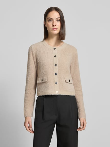 Frauenmodel trägt Strickjacke mit Boucléstruktur von Betty Barclay in Beige mit Zierknöpfen und Pattentaschen, Ganzkörperansicht von vorne.