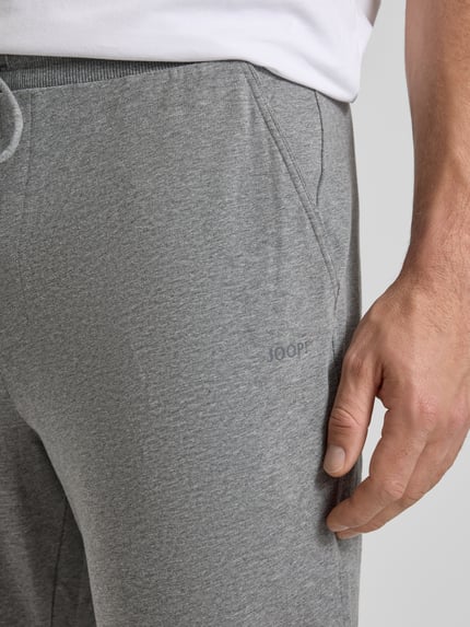Mężczyzna nosi Sweatpants mit elastischem Bund und Tunnelzug od JOOP! Collection, bawełniany materiał z domieszką stretchu, krój regular fit, szary kolor, zbliżenie na biodro.