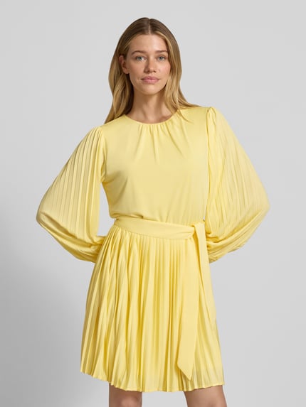 Frauenmodel trägt Cocktailkleid mit Plisseefalten Modell 'Celina' von GUIDO MARIA KRETSCHMER WOMAN, taillierter Schnitt, Minikleid, Gelb, Ganzkörperansicht von vorne.