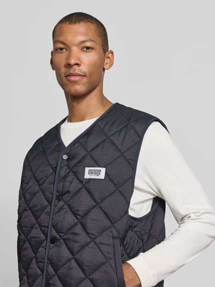 Männermodel trägt dunkelblaue Weste mit Label Patch Modell 'YUPIBAM' von AMERICAN VINTAGE, Rautenstruktur, Nahaufnahme Oberkörper.