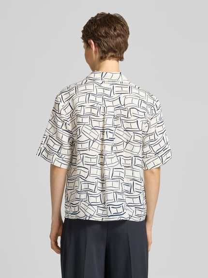 Männermodel draagt Loose Fit linnen blouse met borstzak van Tommy Hilfiger, all-over motief, overhemdkraag, korte mouw, gestikt logo, achterpas met cacharelvouw, knoopsluiting, materiaal: puur linnen. Ganzkörperansicht Rückansicht.