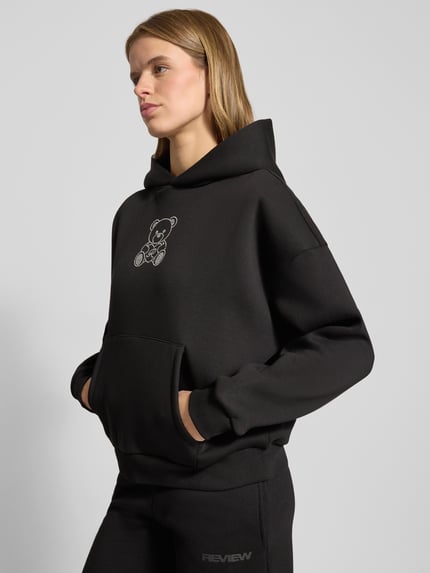 Frauenmodel trägt Hoodie mit Kapuze von Review im Baumwoll-Mix, locker geschnitten, Ziersteinbesatz, Känguru-Tasche, Nahaufnahme Oberkörper.