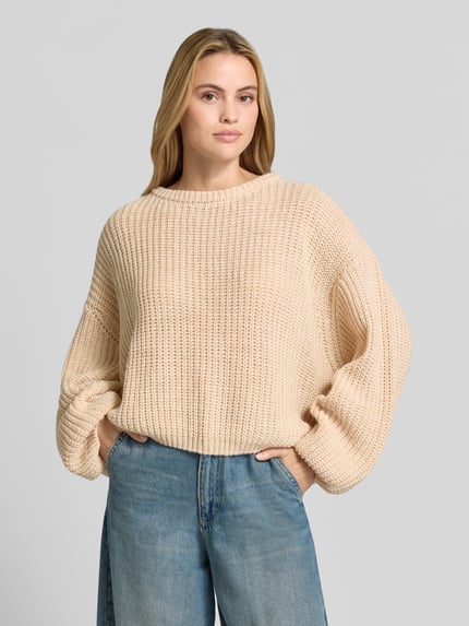 Frauenmodel trägt Oversized Strickpullover aus Leinen-Mix von American Vintage in Beige, grob gestrickt, mit Rundhalsausschnitt, Nahaufnahme Oberkörper.