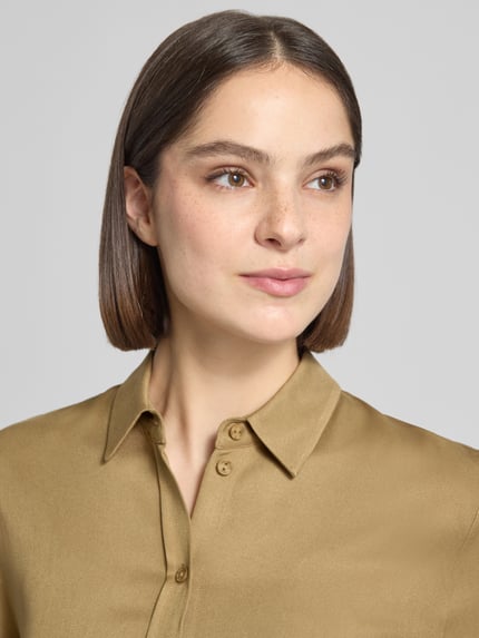 Frauenmodel trägt Kurzarmbluse aus Viskose mit 1/2-Arm von JAKE*S STUDIO WOMAN in schlankem Schnitt, Kentkragen, Nahaufnahme Oberkörper. Rückenlänge 54 cm, Ärmellänge 29 cm, Farbe einfarbig in warmem Goldton mit glatter Textur.