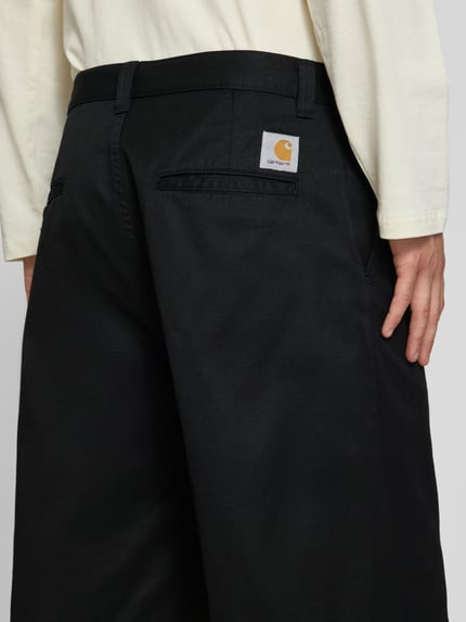 Männermodel trägt Bermudas mit Baumwoll-Anteil Modell 'Brader' von Carhartt Work In Progress in Schwarz, Material-Mix, Relaxed Fit, Nahaufnahme Rückansicht.