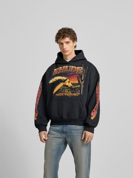 Männermodel trägt Hoodie mit Kapuze von RHUDE aus Reine Baumwolle, Lockerer-Schnitt, Label-Print, Känguru-Tasche, Ganzkörperansicht von vorne. Rückenlänge bei Größe M: 61 cm.