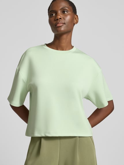 Frauenmodel trägt Boxy Fit Sweatshirt aus Viskose-Mix mit 1/2-Arm von MSCH Copenhagen in hellem Grün, Rundhalsausschnitt, Stretch-Anteil, Modell 'Nilda Ima', glatte Textur, Ganzkörperansicht von vorne.